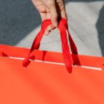 Customer Segmentation - High angle of crop anonymous female buyer taking red paper bag with purchase in sunshine