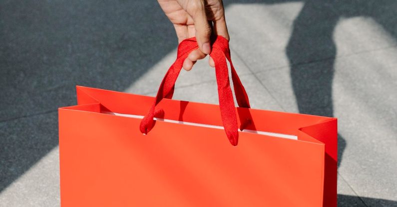 Customer Segmentation - High angle of crop anonymous female buyer taking red paper bag with purchase in sunshine