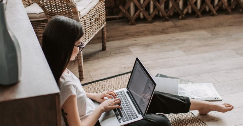 Referral Programs - Young barefoot woman using laptop on floor near books in stylish living room