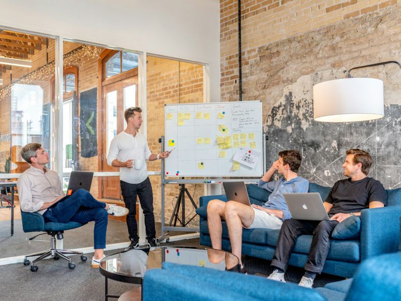 KPIs - three men sitting while using laptops and watching man beside whiteboard